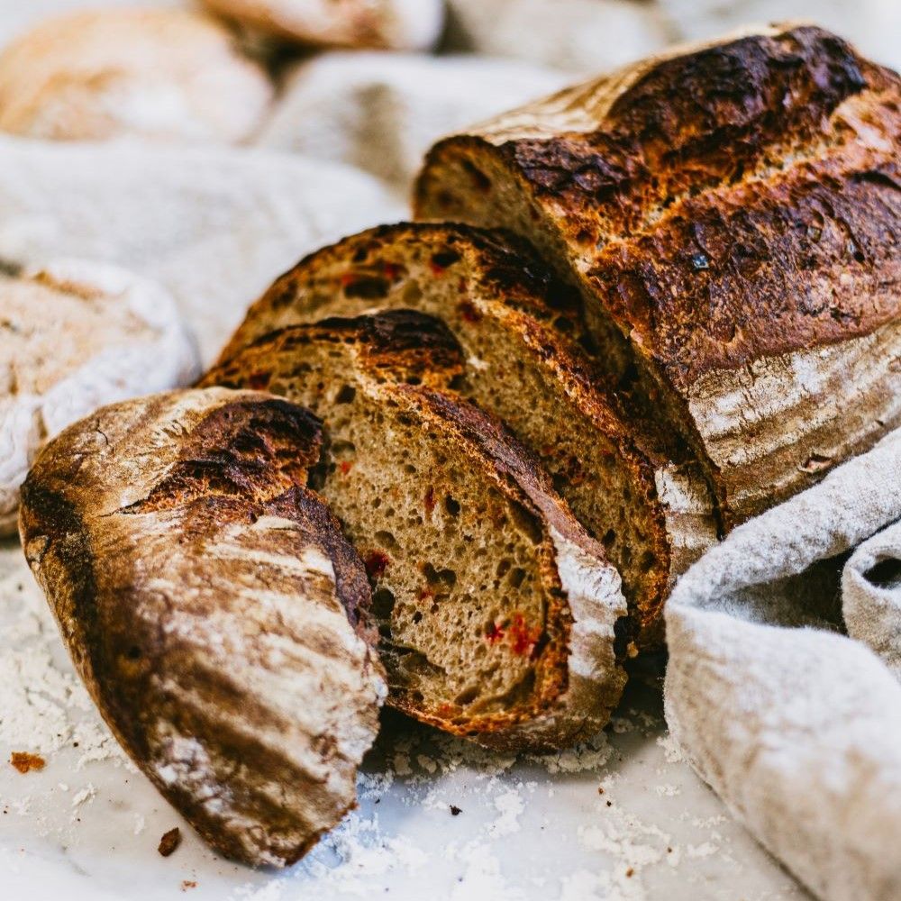 Geschnittenes Brot, Kruste dunkelbraun. Einige Scheiben liegen neben dem Laib. Auf hellem Untergrund.
