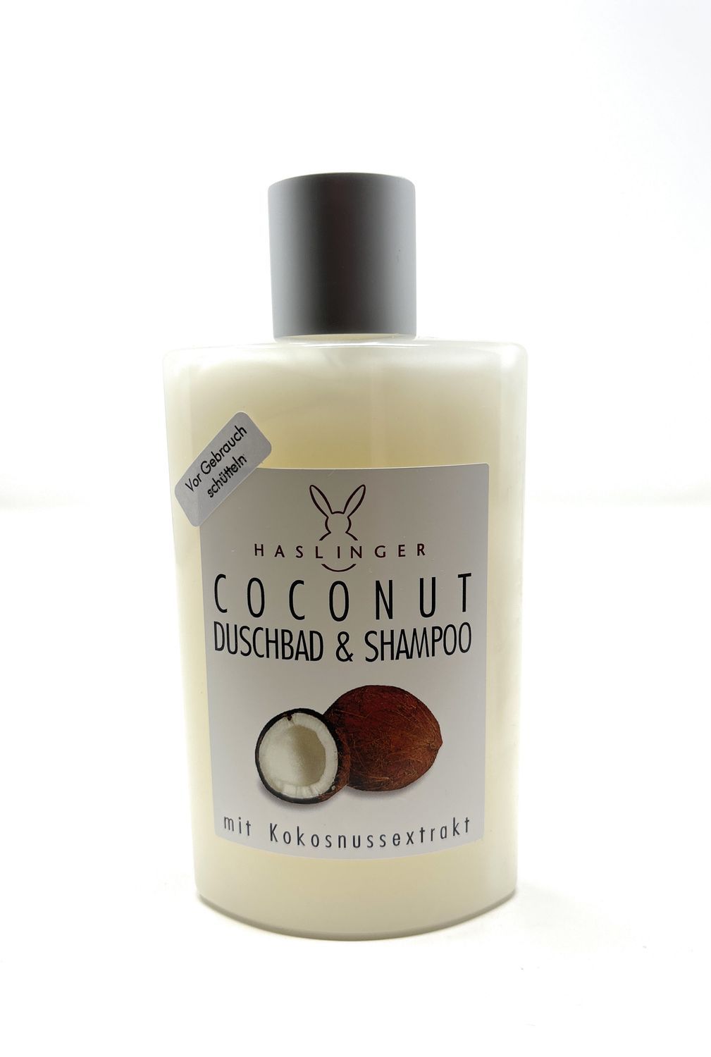 Flasche Haslinger Coconut Duschbad & Shampoo. Weißes Etikett mit Kokosnuss-Illustration und Text. Grauer Deckel.