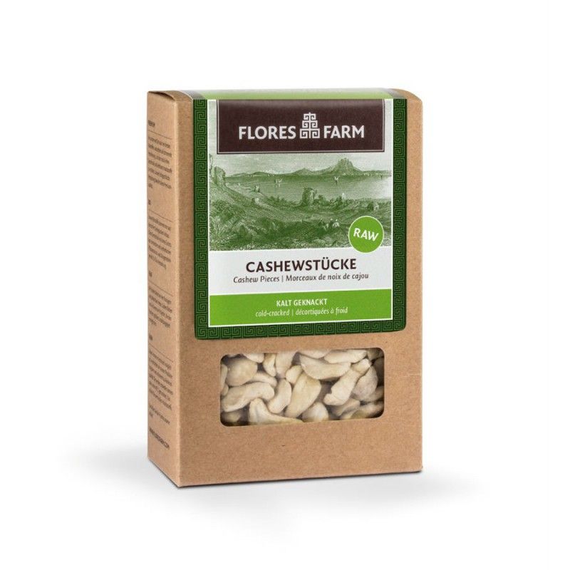 Kartonverpackung mit Cashewkernen. Sichtfenster zeigt Cashewstücke. Logo: Flores Farm. Text: Cashewstücke, kalt geknackt.