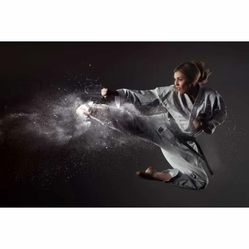 Eine Person in einem Karate-Anzug führt einen Tritt aus, umgeben von Staubwolken.