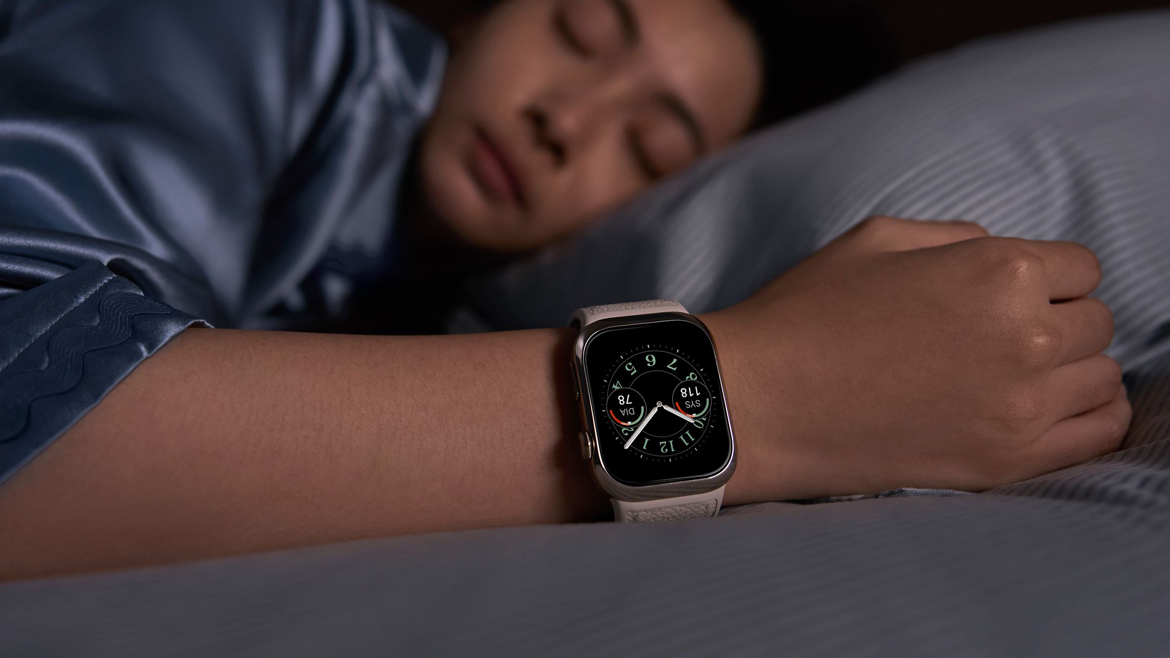 Person mit Smartwatch am Handgelenk, liegend im Bett. Das Display zeigt Gesundheitsdaten.