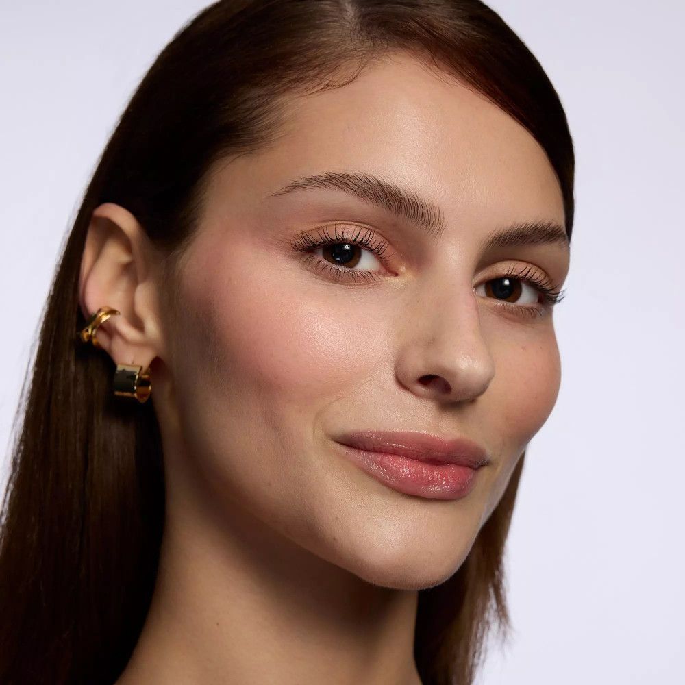 Porträt einer Frau mit hellem Teint. Sie trägt goldene Ohrringe. Ungeschminkte Lippen.