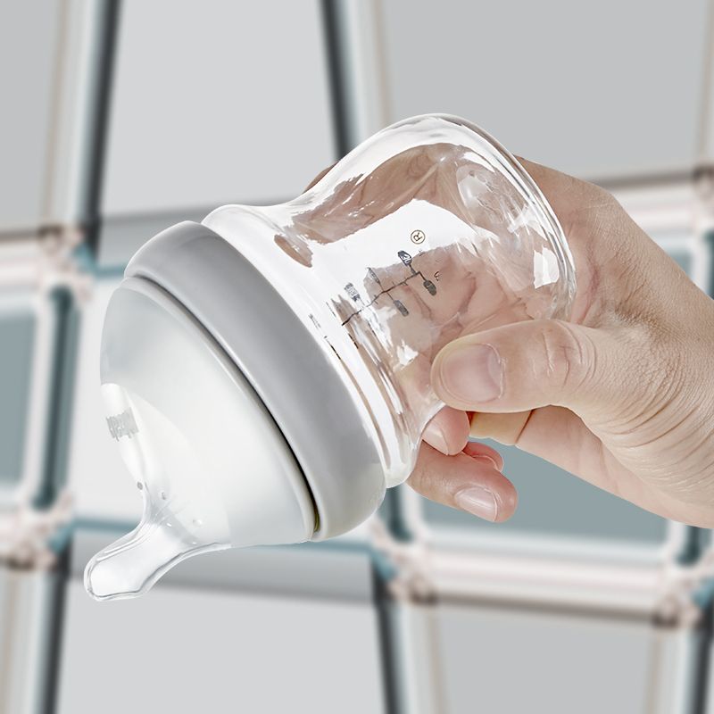 Glasflasche mit grauem Ring und Sauger. Hand hält Flasche. Messskala auf der Flasche.