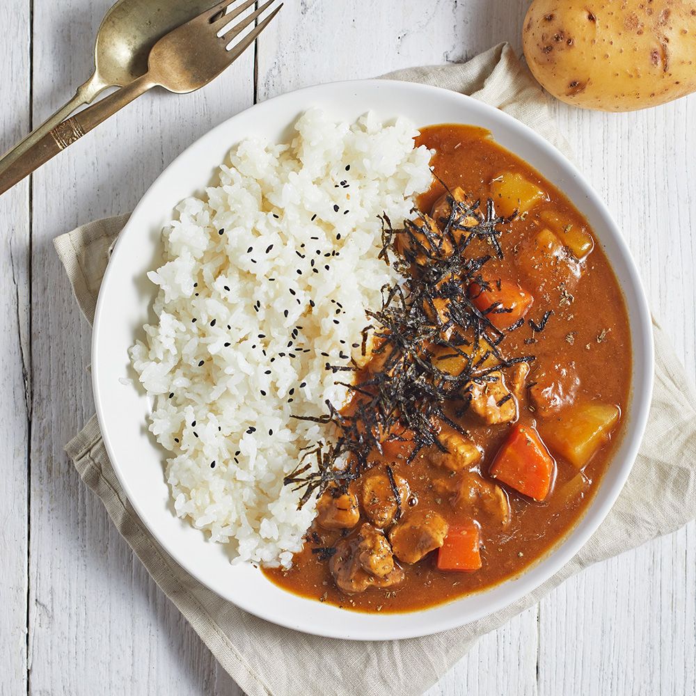 Teller mit Reis und Curry. Curry mit Fleisch, Kartoffeln und Karotten. Garniert mit Algen.