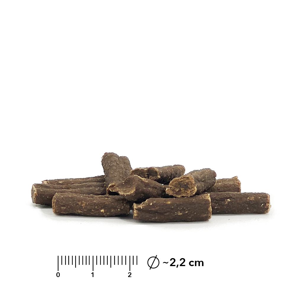Haufen von zylindrischen, braunen Snacks. Durchmesser ca. 2,2 cm. Auf weißem Hintergrund.