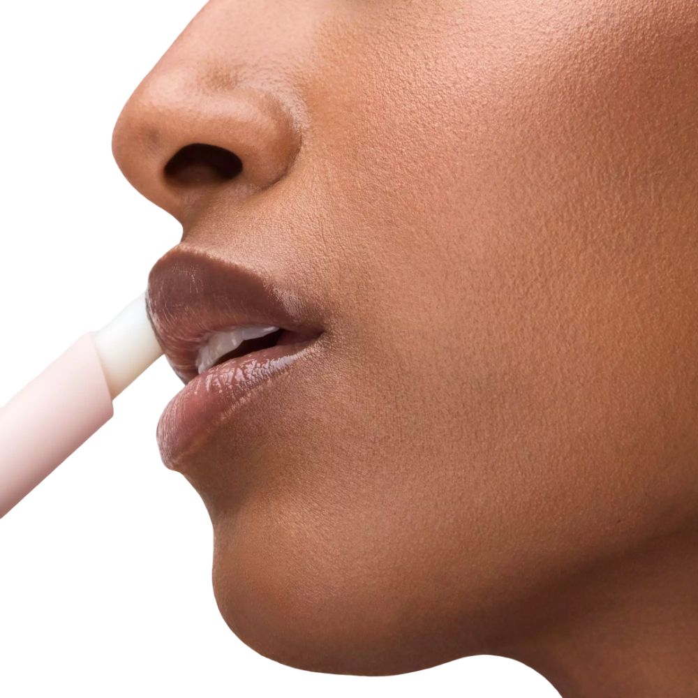 Nahaufnahme einer Person, die einen hellrosa Lippenbalsam auf die Lippen aufträgt.