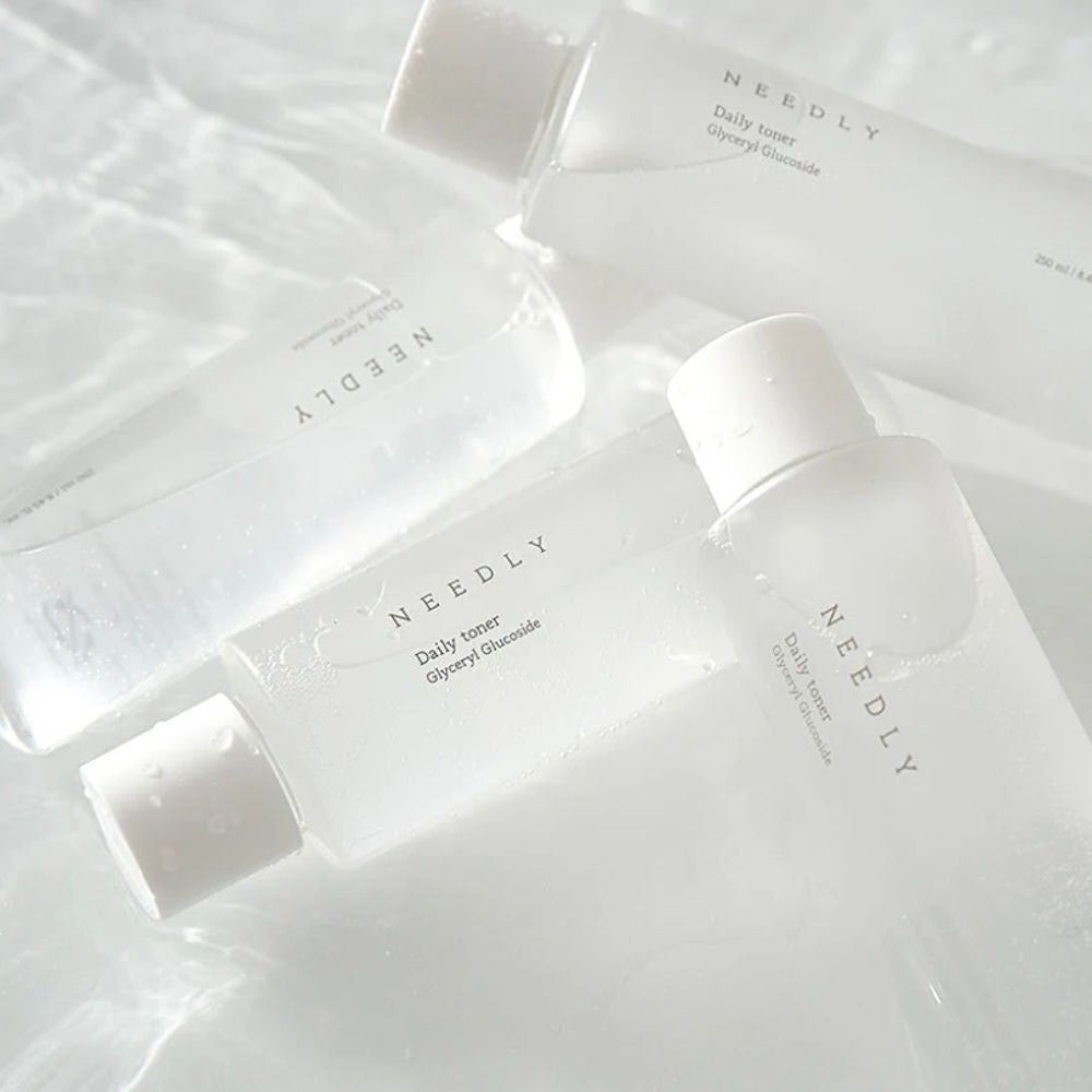 Mehrere Flaschen mit weißem Deckel. Aufschrift: NEEDLY Daily Toner. Klarer Inhalt.