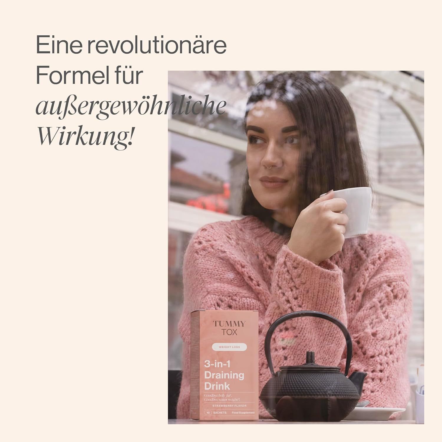 Frau sitzt an einem Tisch und hält eine Packung "Tummy Tox 3-in-1 Draining Drink". Auf dem Tisch steht eine Teekanne.