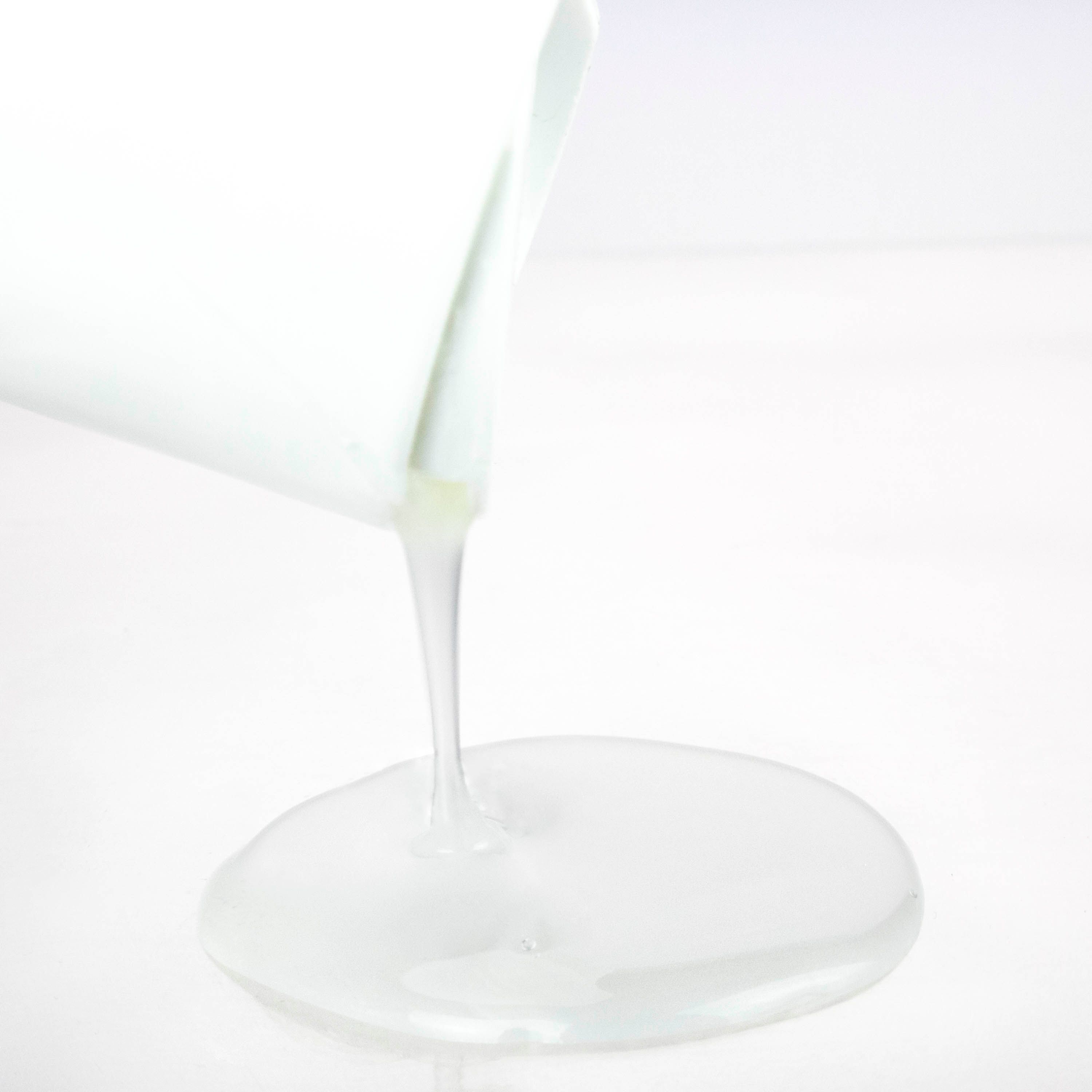 Flüssigkeit fließt aus einer weißen Flasche. Die Flüssigkeit ist weiß und bildet einen flachen Pool auf einer weißen Oberfläche.