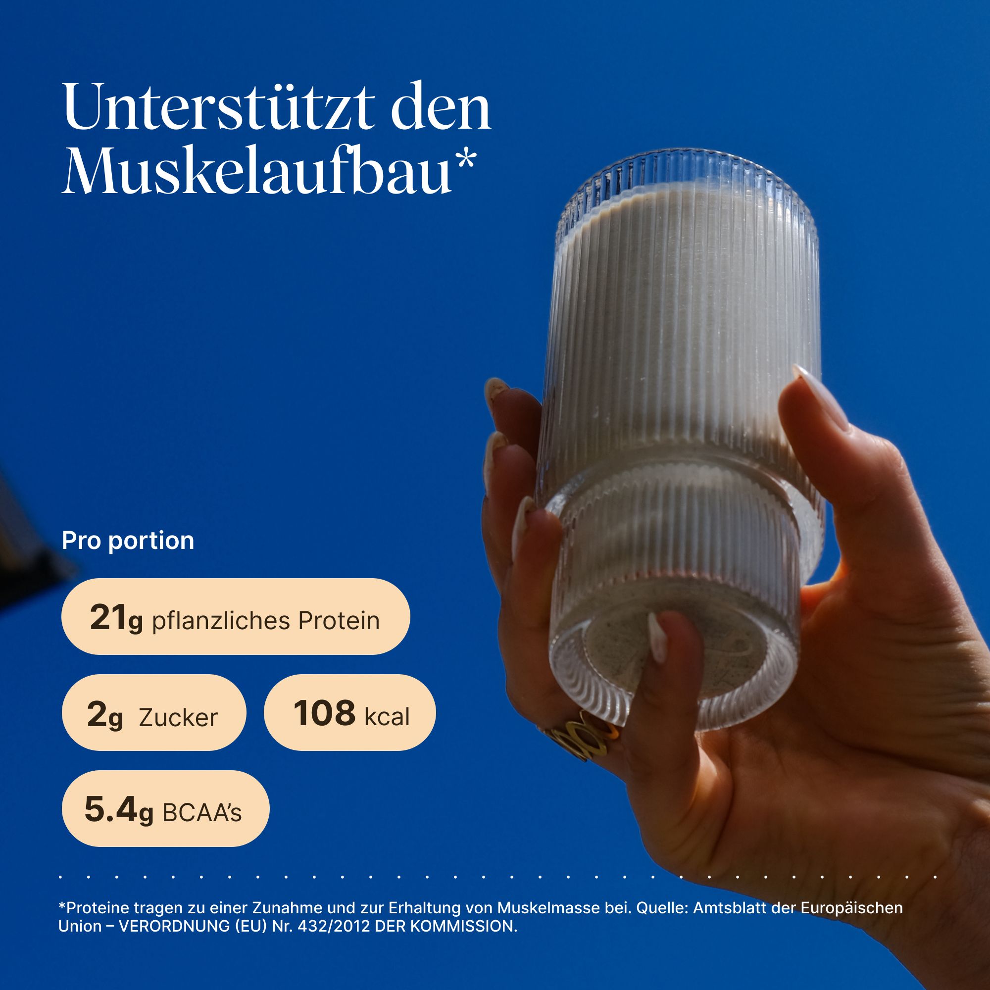 Glas mit Proteinshake, gehalten von einer Hand. Aufschrift: 21g pflanzliches Protein, 2g Zucker, 108 kcal, 5.4g BCAAs. Hintergrund: blauer Himmel.