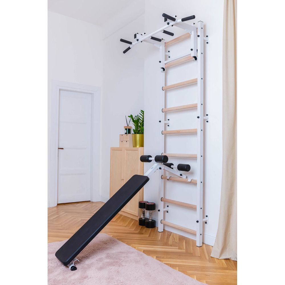Fitness-System mit Sprossenwand, Klimmzugstange, Dip-Barren und Trainingsbank. In einem Raum, neben einer Tür.