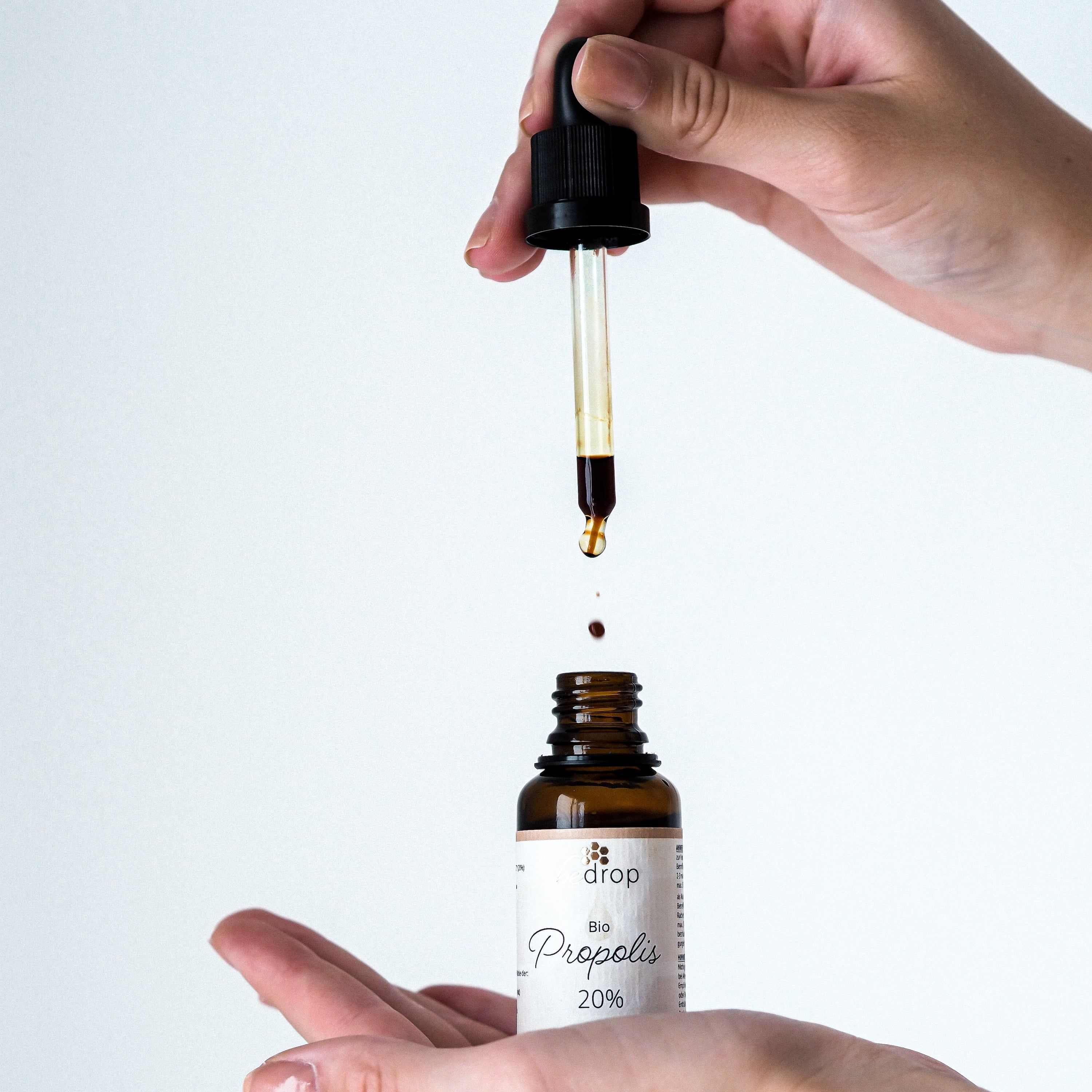 Braune Glasflasche mit Pipette. Tropfen Propolis-Extrakt. Hände halten Pipette und Flasche.