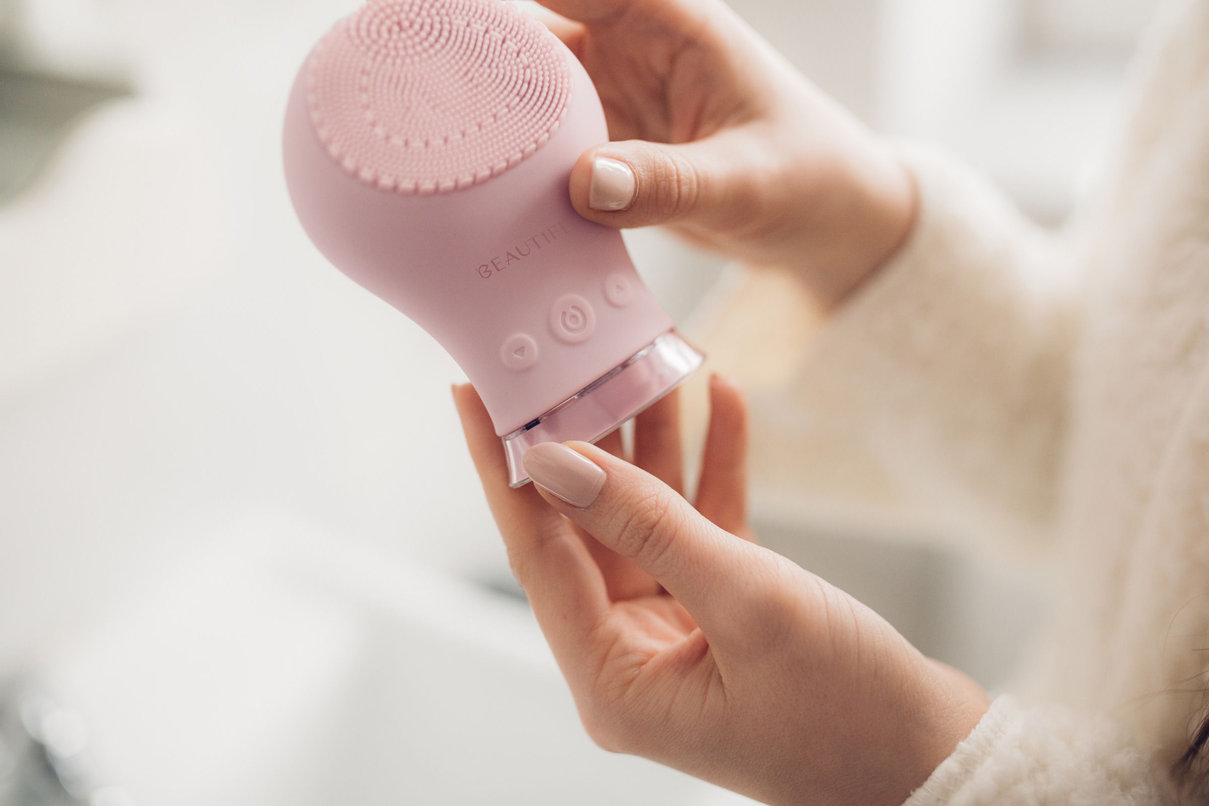 Hände halten rosa Schall-Gesichtsbürste. Borstenbereich sichtbar. Helle Umgebung.