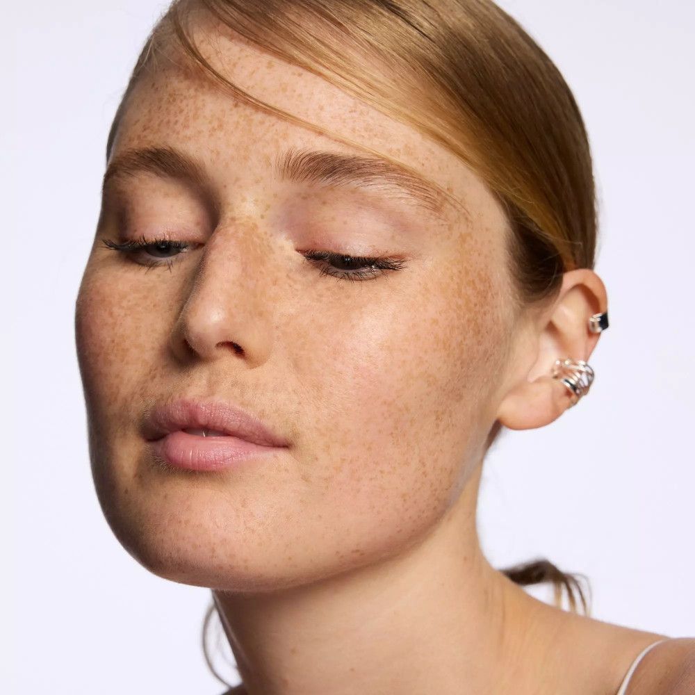 Porträt einer jungen Frau mit Sommersprossen und auffälligem Ohrschmuck. Sie trägt dezentes Make-up.
