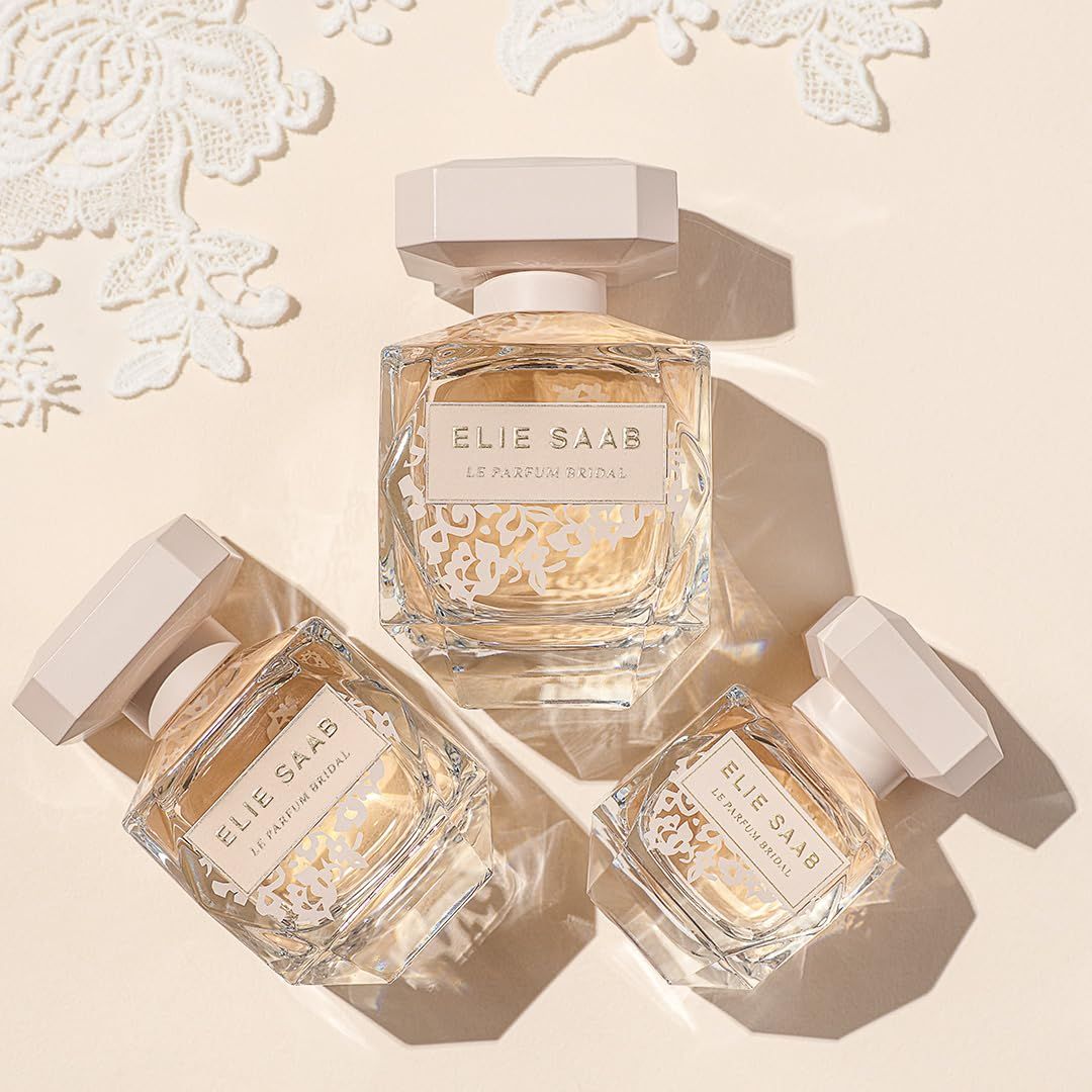 Drei Flakons. Aufschrift: Elie Saab Le Parfum Bridal. Floral-Dekor. Beige Hintergrund.
