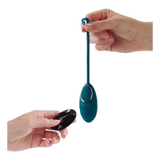 Türkisfarbener Vibrator mit Fernbedienung. Ovaler Kopf, goldfarbener Ring, schwarze Fernbedienung. Hände halten die Teile.