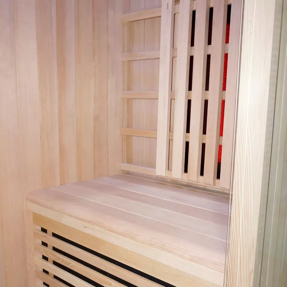 Innenansicht der Infrarotsauna. Holzkonstruktion mit Sitzbank und Rückenlehne. Roter Infrarotstrahler sichtbar.