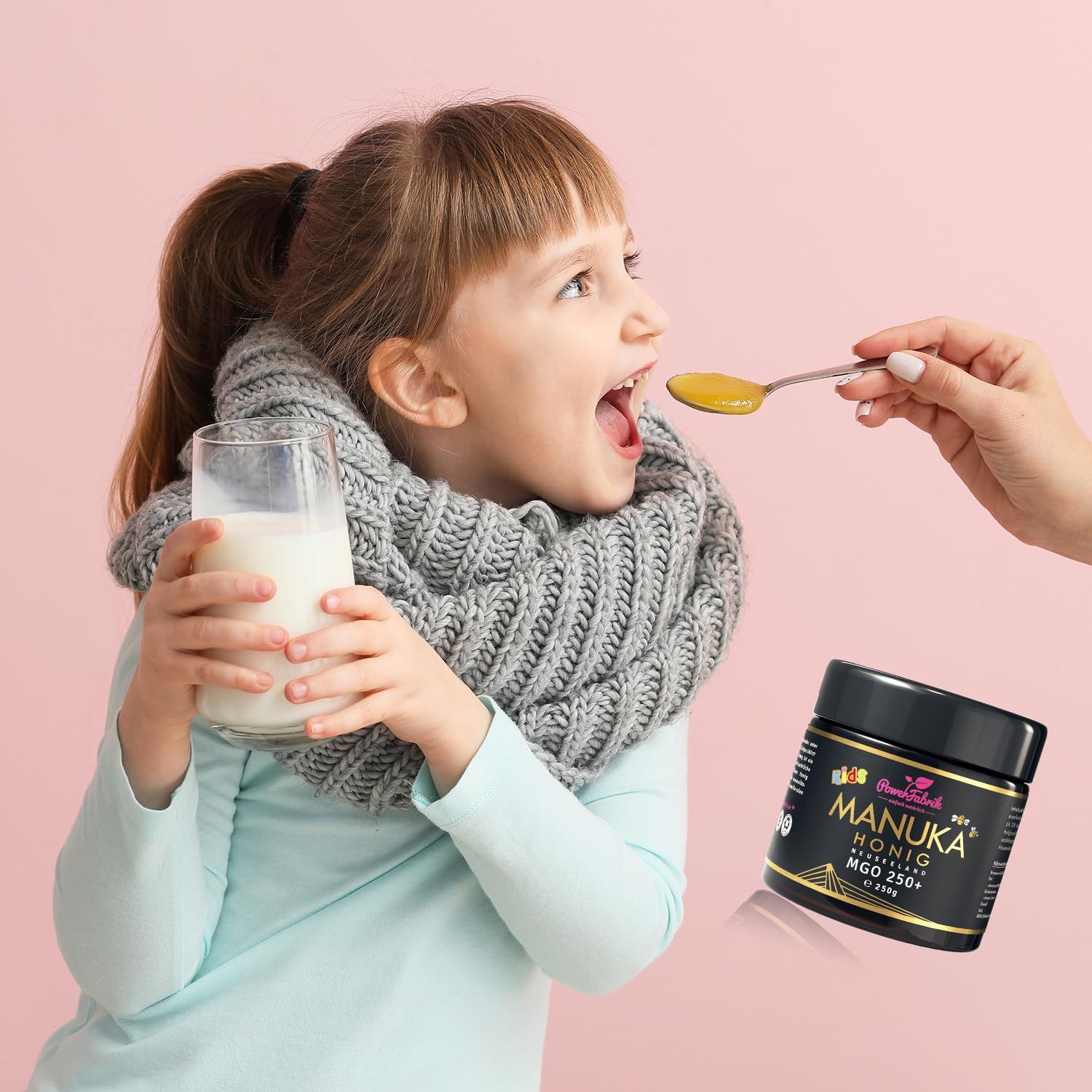 Kind bekommt mit einem Löffel Honig in den Mund gefüttert. Glas Manuka Honig, MGO 250+ daneben, Glas Milch.