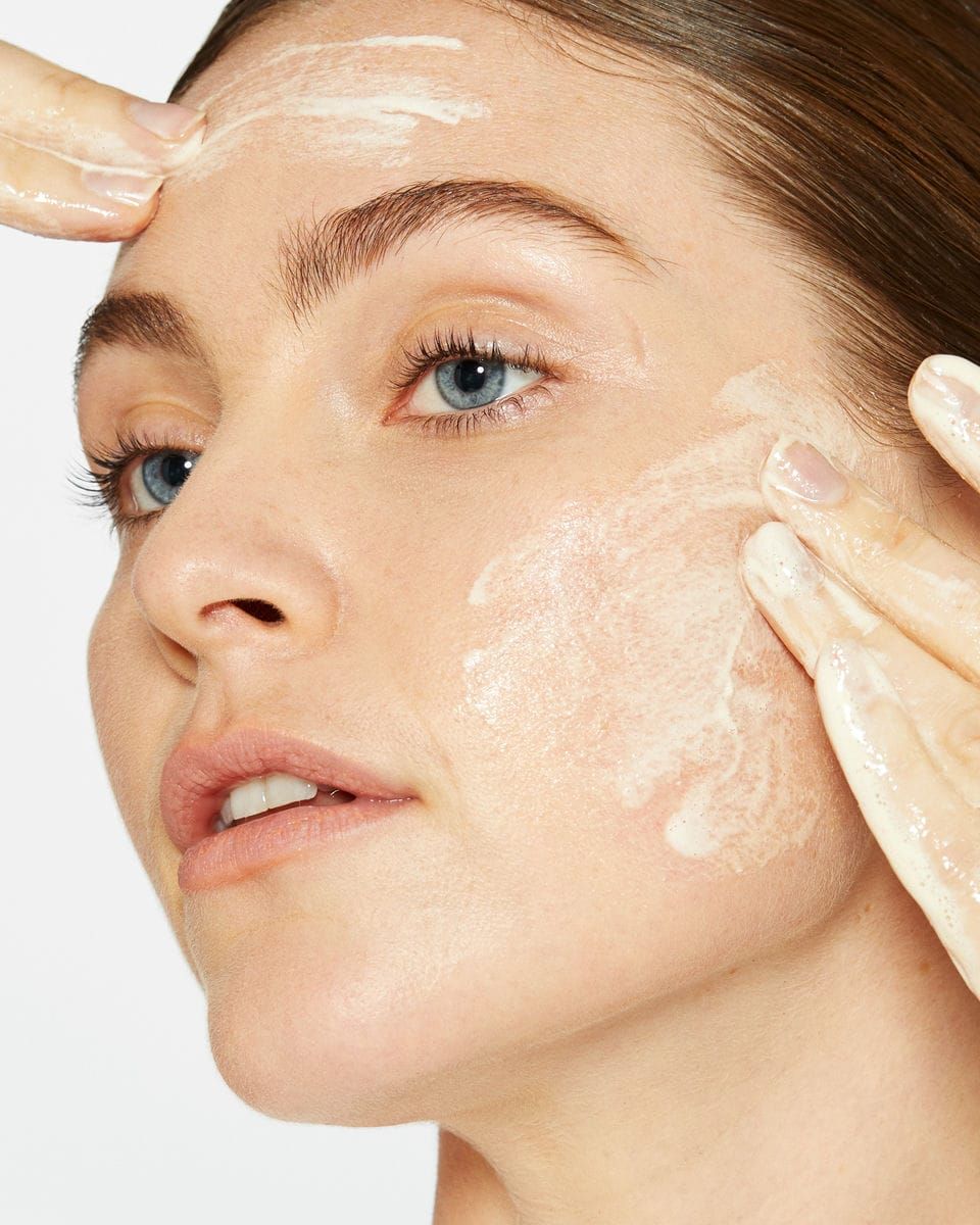 Frau, die ein Produkt auf ihr Gesicht aufträgt. Hände verteilen eine cremige Substanz.