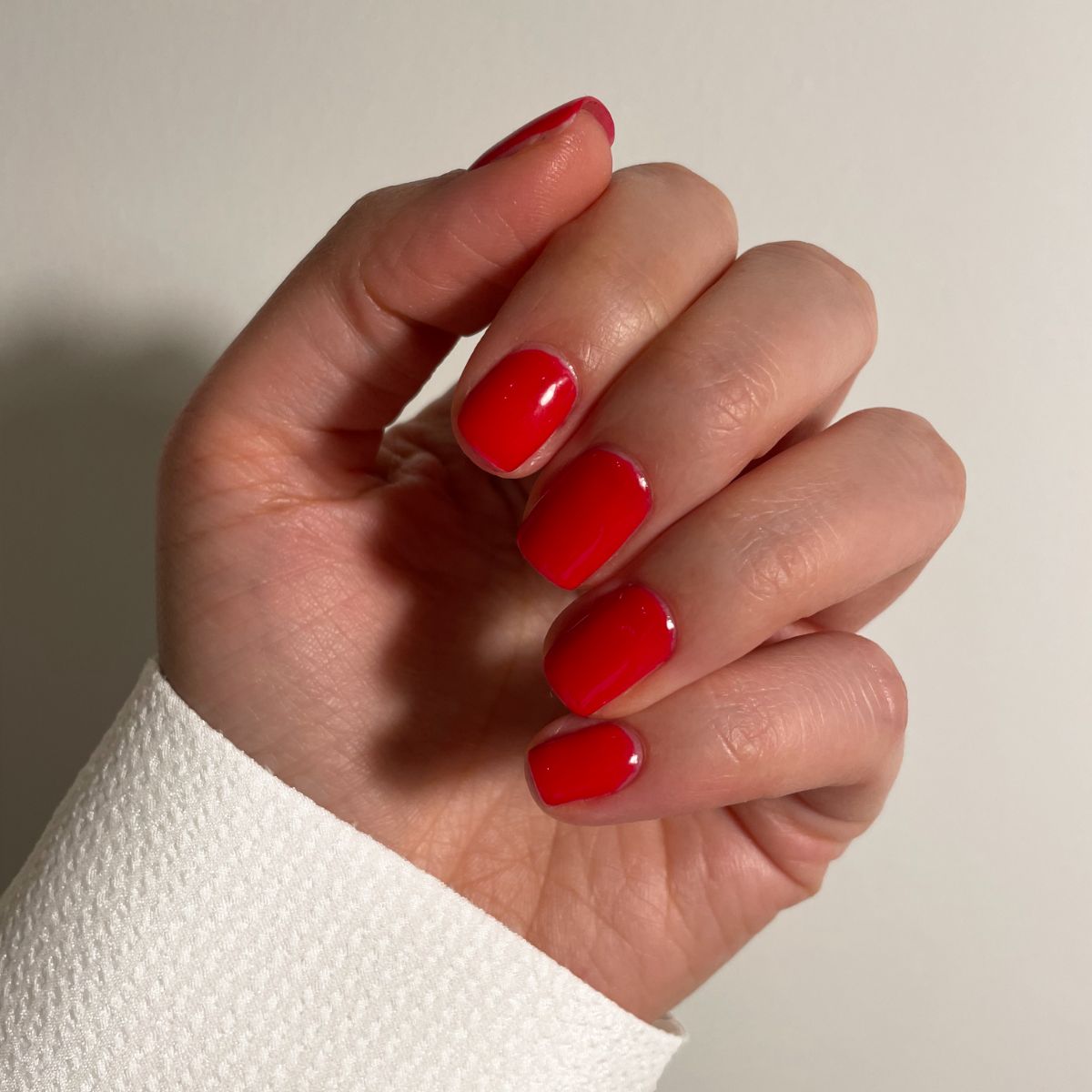 Hand mit roten, lackierten Nägeln. Die Nägel sind kurz und glänzend. Der Hintergrund ist weiß.