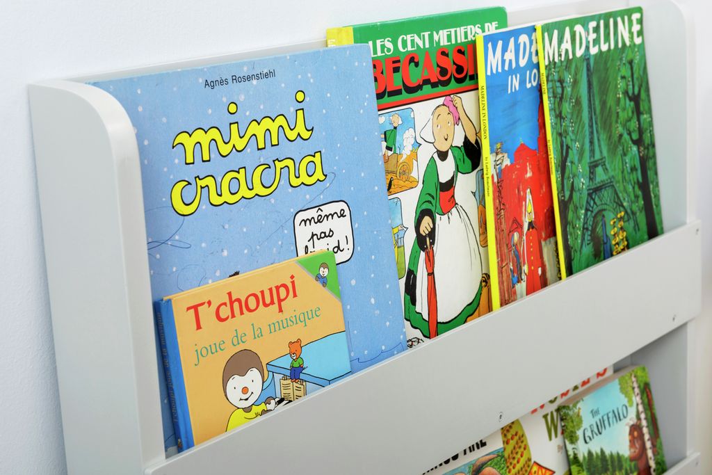 Hellgraues Bücherregal mit Büchern. Bücher mit farbigen Einbänden. Bücher mit Titeln wie "Mimi Cracra" und "Madeline in Love".