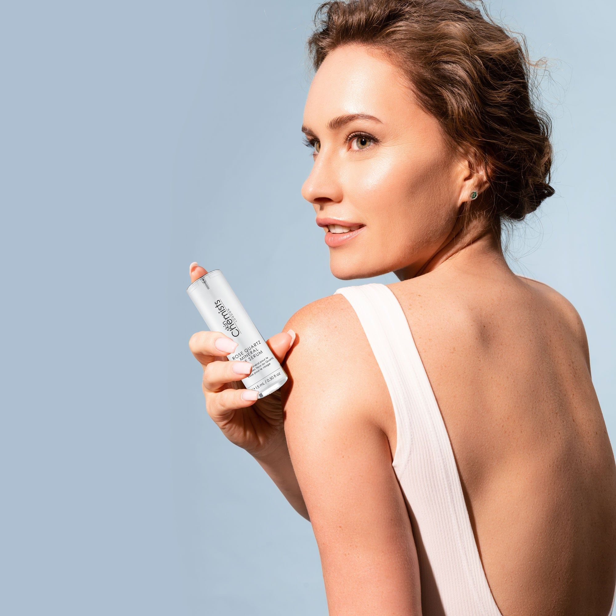 Frau mit Serum auf der Haut. Flasche mit Aufschrift: Rose Quartz Mineral Eye Serum. Marke: skinChemists London. Volumen: 15 ml / 0.50 fl oz.