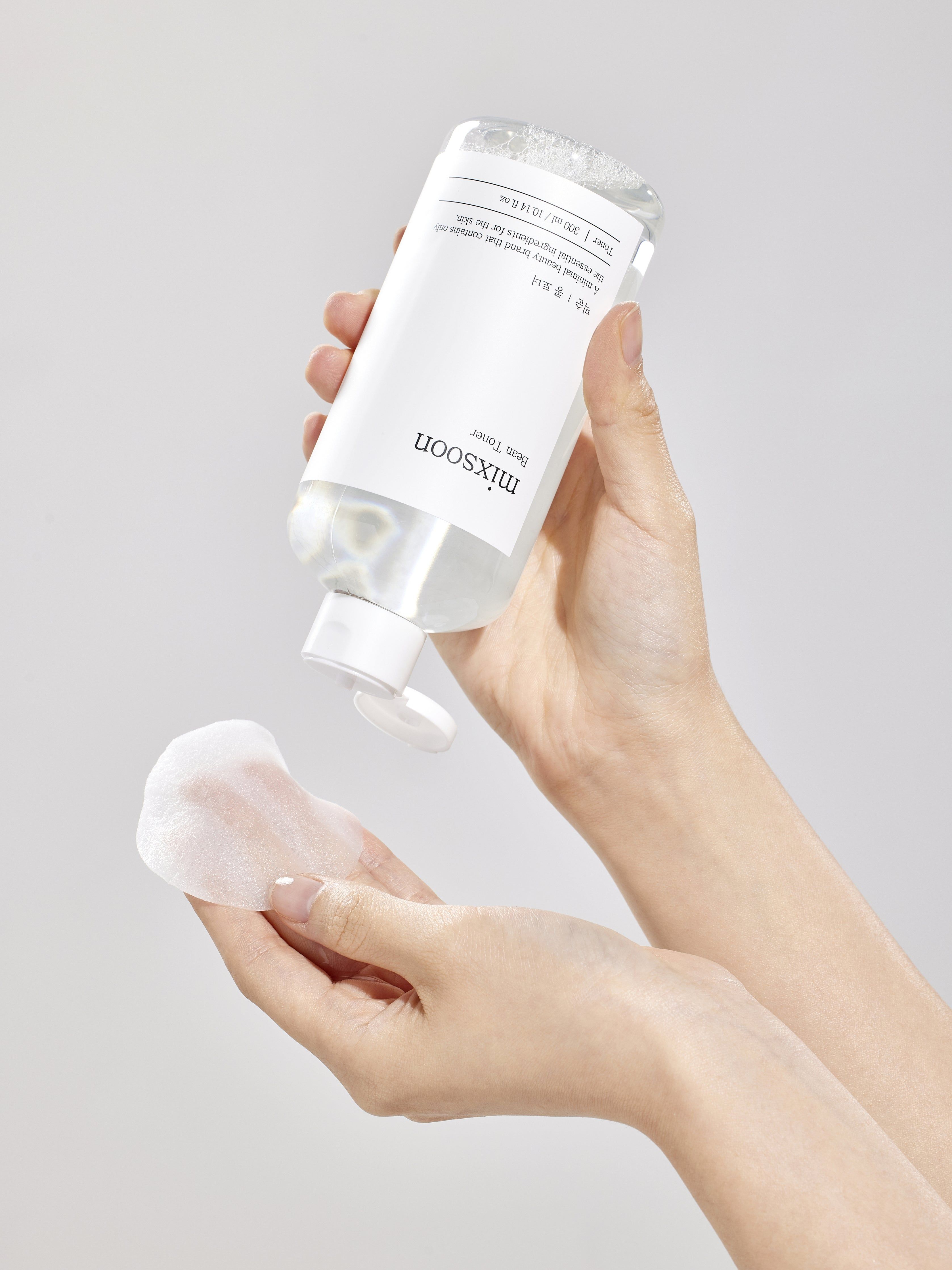 Hände halten eine Flasche mixsoon Bean Toner und ein Wattepad. Toner wird auf das Pad gegossen.