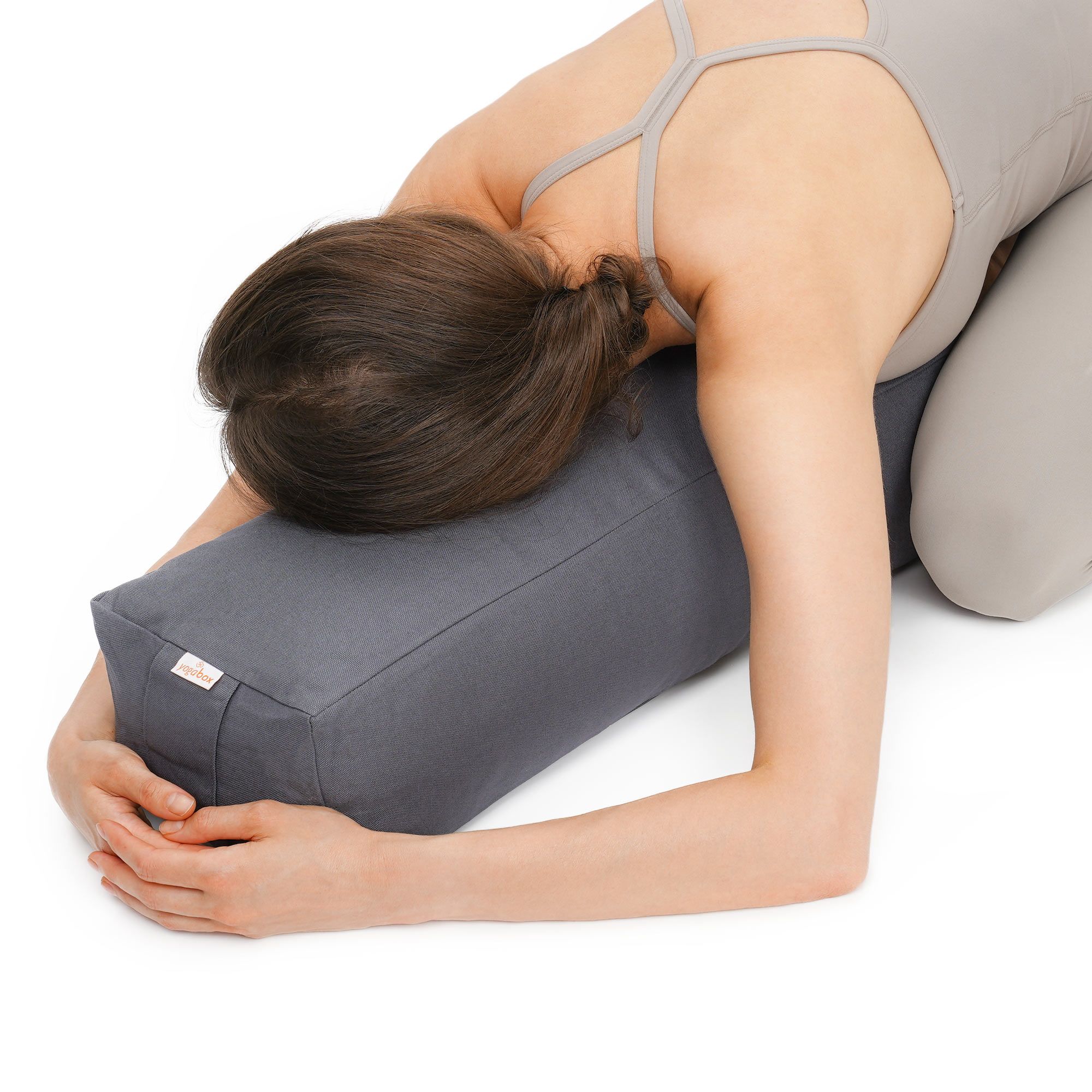 Frau in Yoga-Pose mit Kopf auf grauem Rechteckbolster.