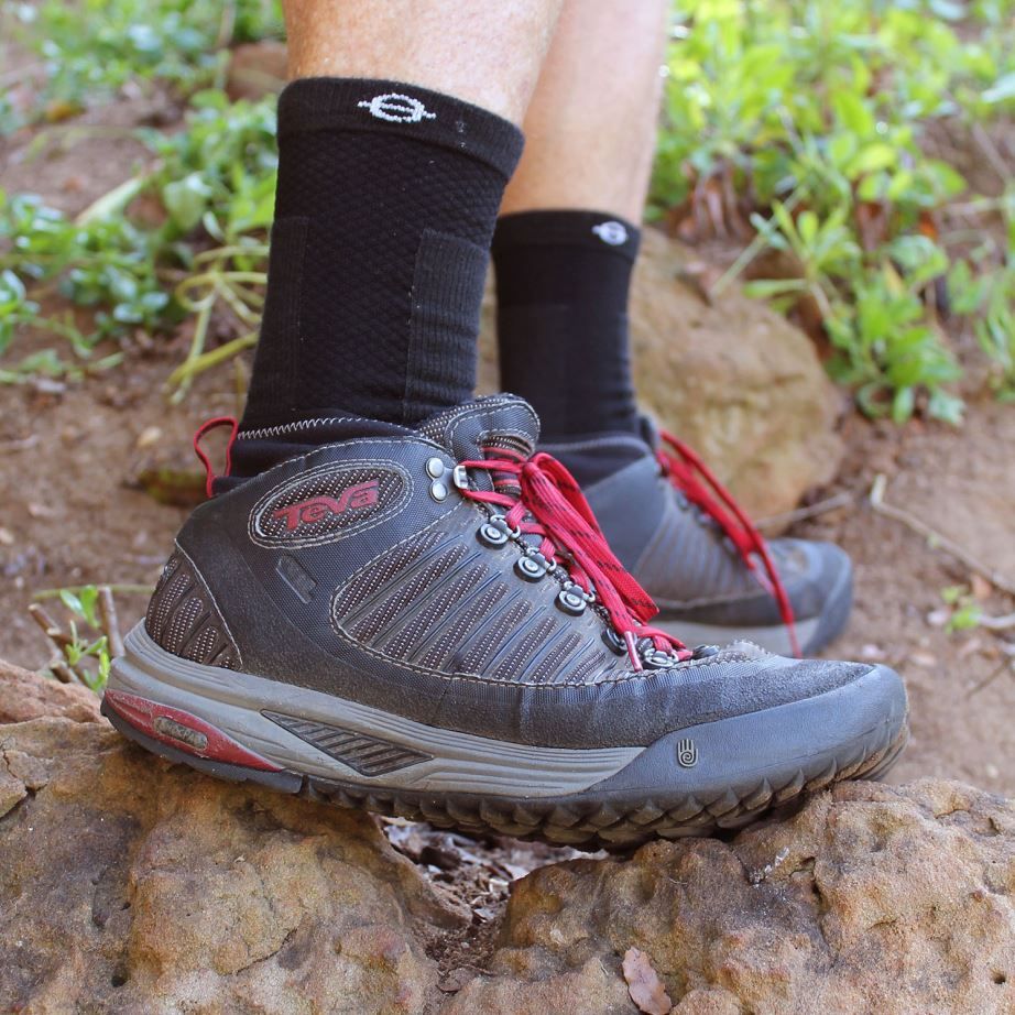 Schwarze Kompressionssocken an Füßen mit Wanderschuhen. Logo am oberen Rand.