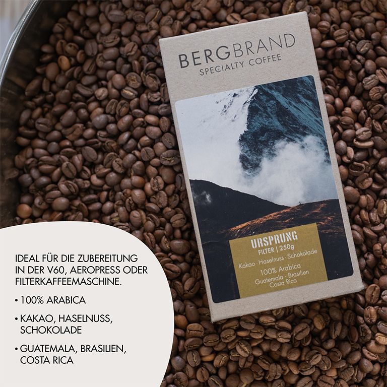 Kaffeebohnen auf einem Tisch. Packung mit Bergmotiv. Text: BERGBRAND, Ursprung, Filter, 250g. Zutaten: Kakao, Haselnuss, Schokolade, 100% Arabica.