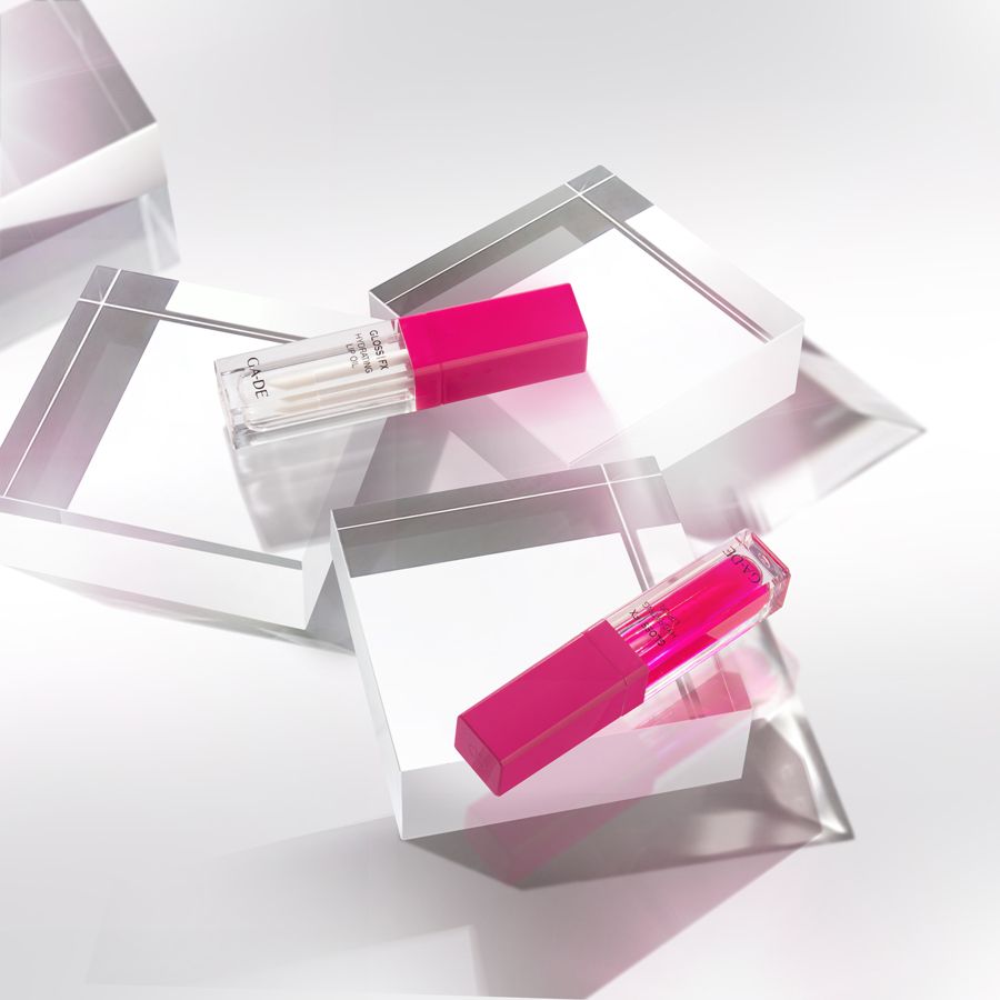 Zwei Ga-De Hydrating Lip Oil-Tuben auf transparenten Würfeln. Pinkfarbene Deckel, transparente Tuben.