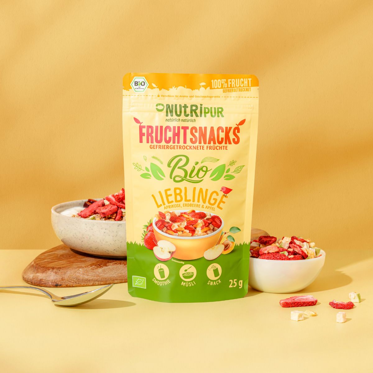 Beutel mit gefriergetrockneten Früchten. Aufschrift: NutriPur, Frucht Snacks, Bio-Lieblinge. Schalen mit Früchten daneben. 25g.