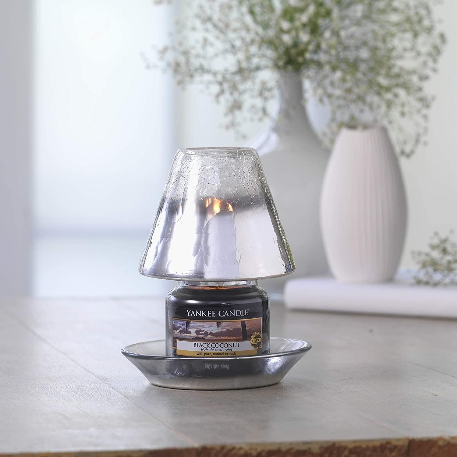 Yankee Candle Black Coconut in Halterung mit Glasaufsatz. Kerze brennt. Auf Tisch mit Vase und Blumen im Hintergrund.