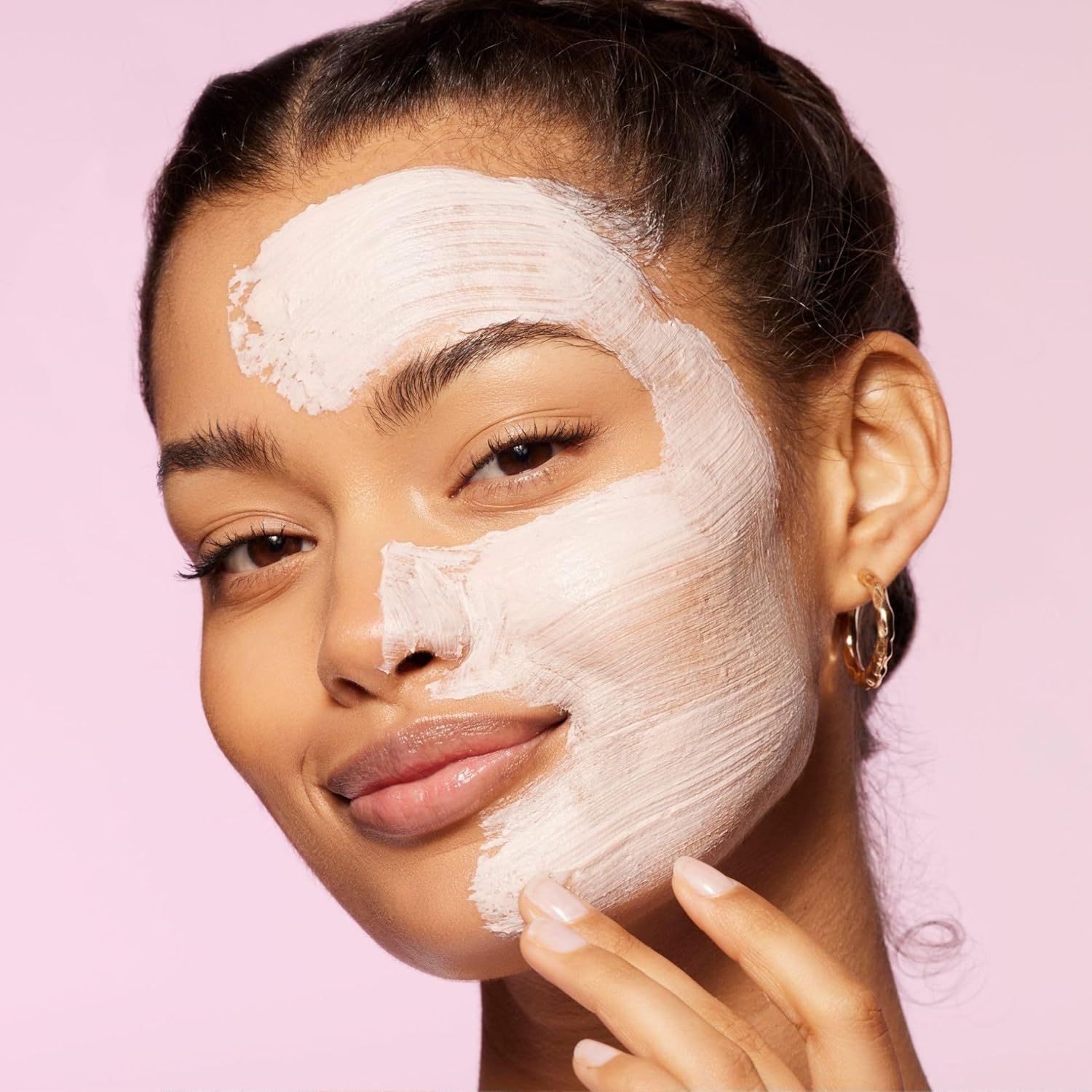 Frau mit Maske auf einer Gesichtshälfte. Maske hell. Hintergrund rosa.