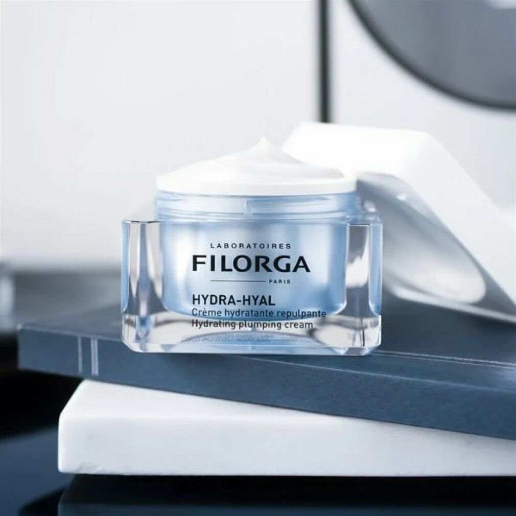 Filorga Hydra-Hyal Creme-Gel. Transparenter Tiegel, blauer Inhalt, weißer Deckel. Auf Büchern.