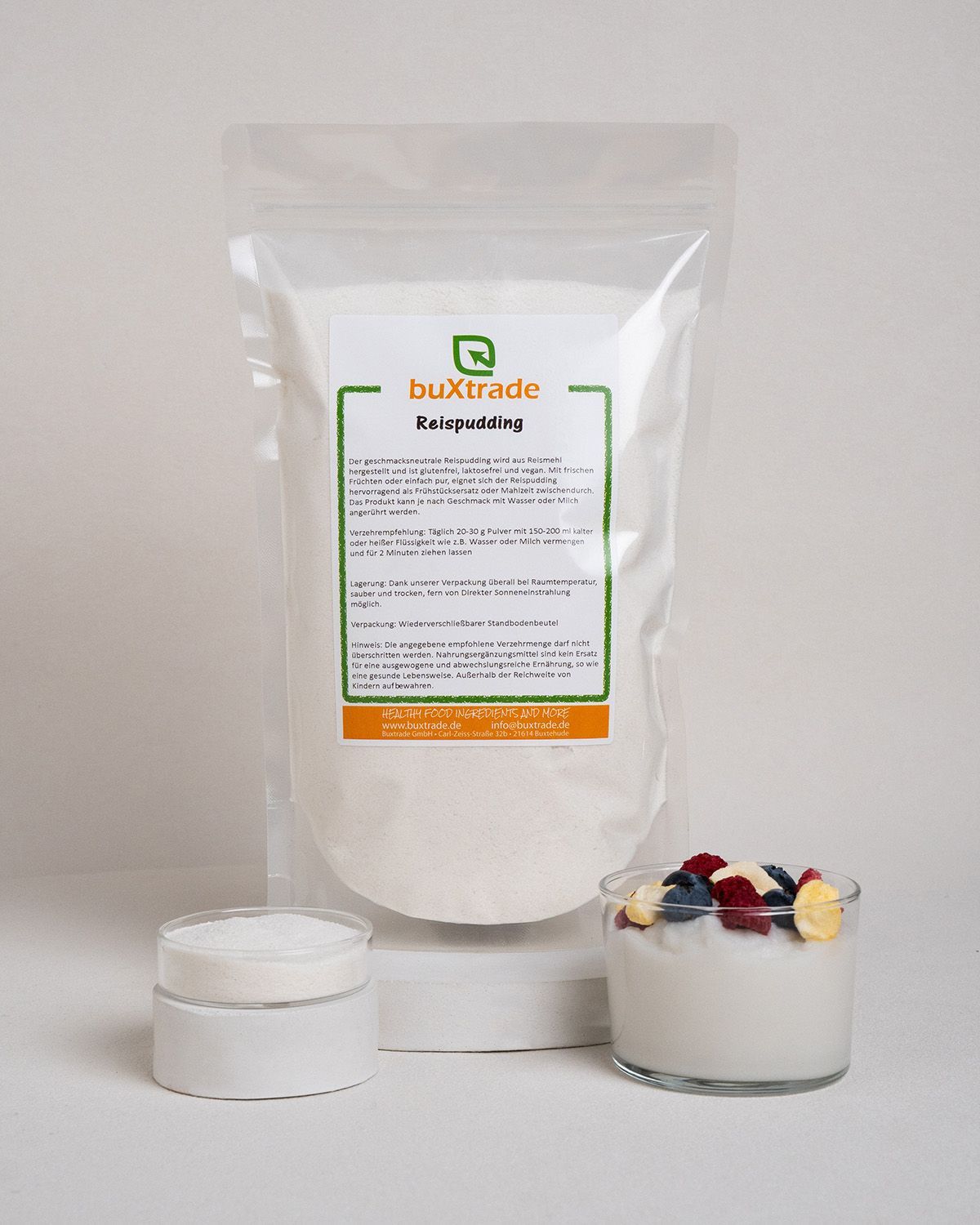 Verpackung mit Reispudding-Pulver, daneben ein Glas mit Pulver und ein Glas mit Pudding, garniert mit Früchten.