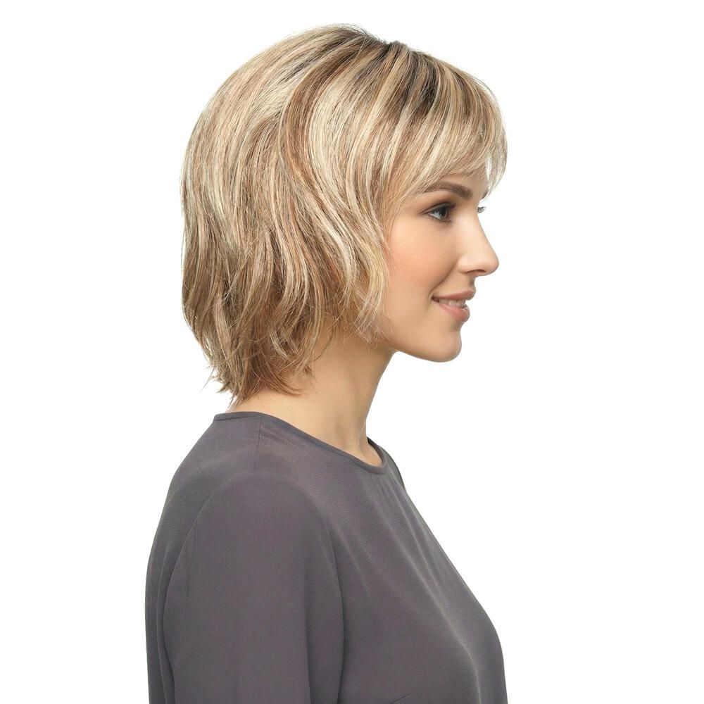 Blonde Perücke, Seitenansicht. Frau mit grauem Oberteil lächelt. Weißer Hintergrund.