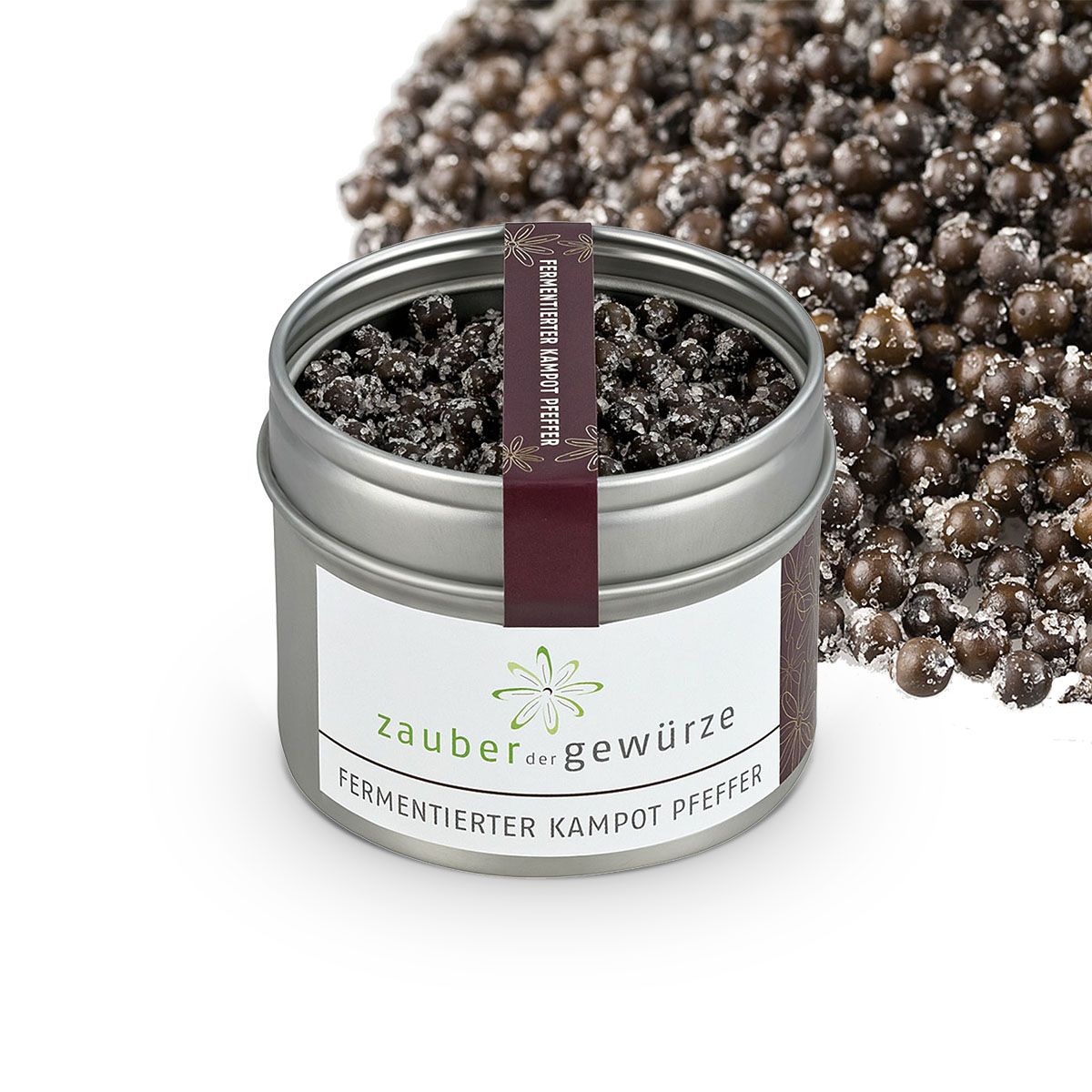 Geöffnete Metallbox mit fermentiertem Kampot Pfeffer. Etikett mit 'Zauber der Gewürze'. Pfefferkörner daneben.