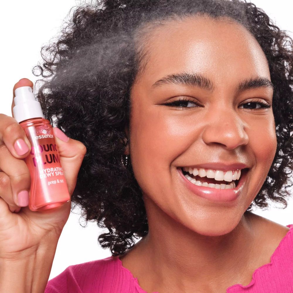 Frau sprüht mit rosa Flasche mit weißem Sprühkopf. Aufschrift: bouncy PLUMP, Hydrating Dewy Spray, prep & set. Marke: essence.