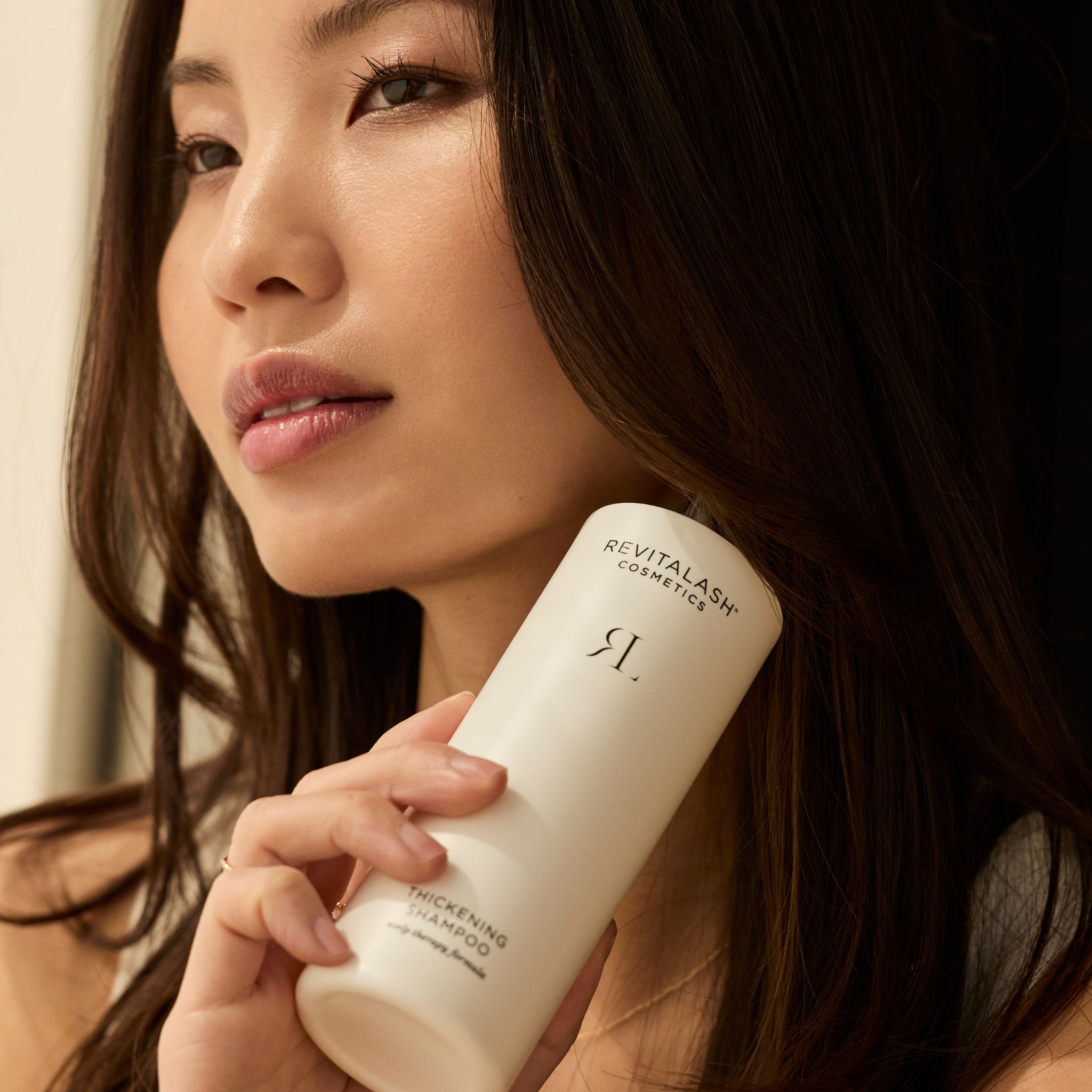 Frau mit langen Haaren hält eine Flasche RevitaLash® Cosmetics Thickening Conditioner.