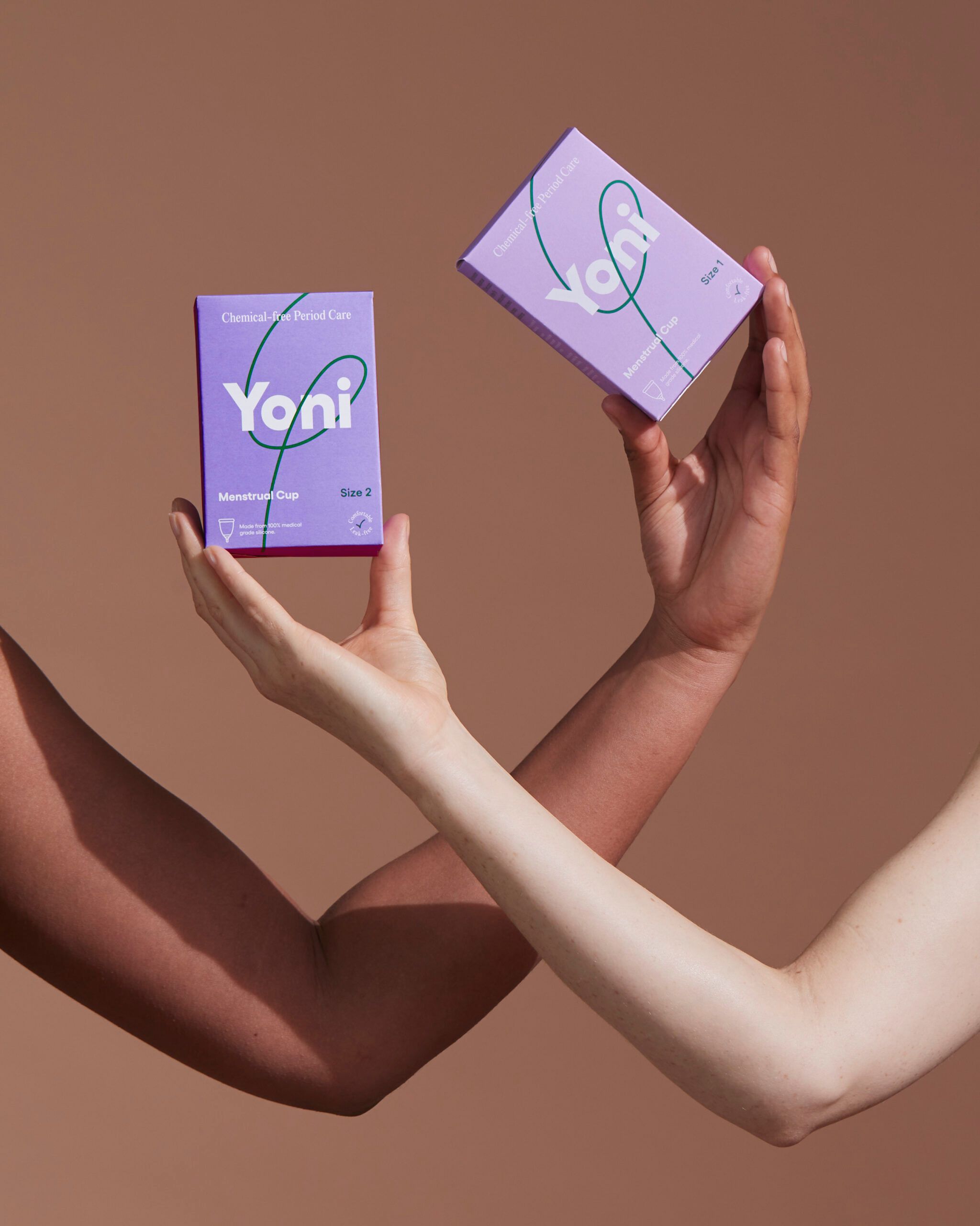 Zwei Hände halten lilafarbene Yoni-Verpackungen. Aufdruck: Yoni, Menstruationstasse, Größe 2.