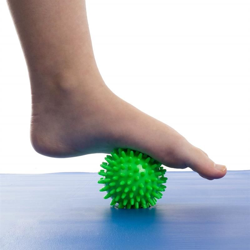 Grüner Massageball mit Noppen unter einem Fuß, der auf einer blauen Matte steht.