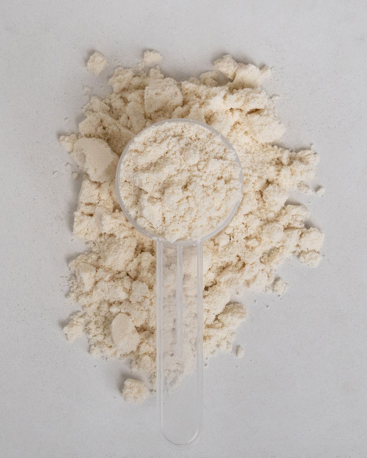 Pulver mit Messlöffel. Helle, beige Pulvermasse. Transparenter Messlöffel.