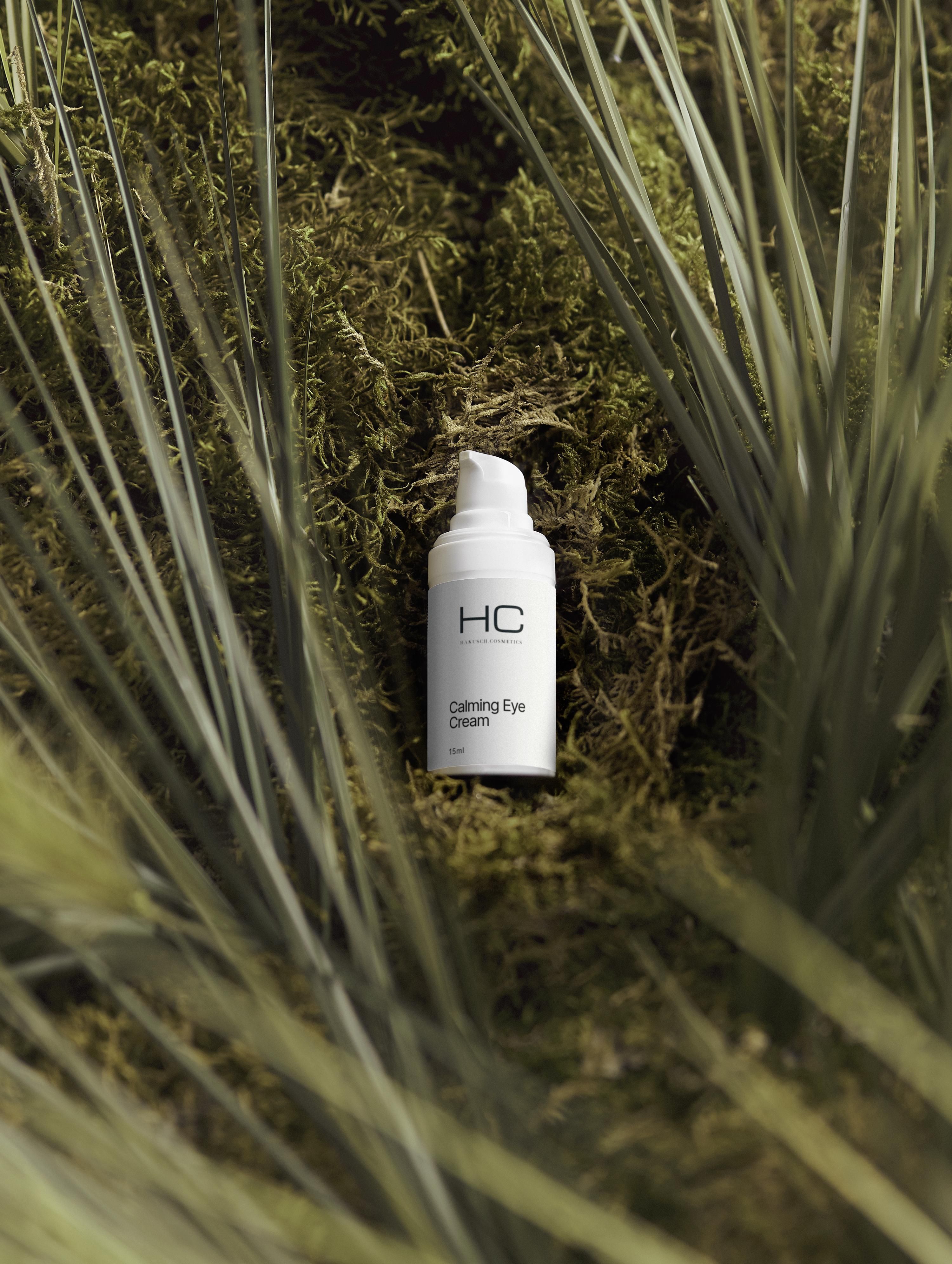 Weiße Flasche "HC Calming Eye Cream" auf Moos. Grüne Pflanzen im Hintergrund.