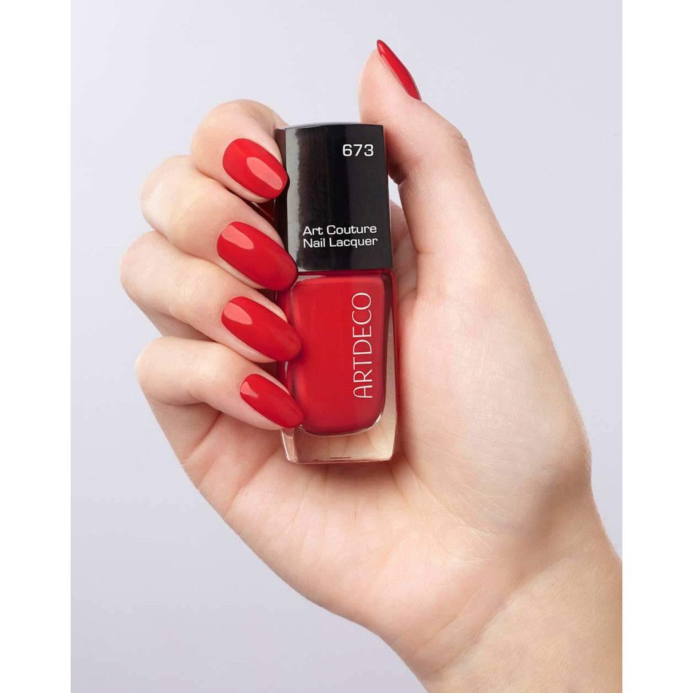 Rote Artdeco Nagellackflasche in Hand. Auf Nägeln und Flasche. Aufschrift: Art Couture Nail Lacquer, 673.