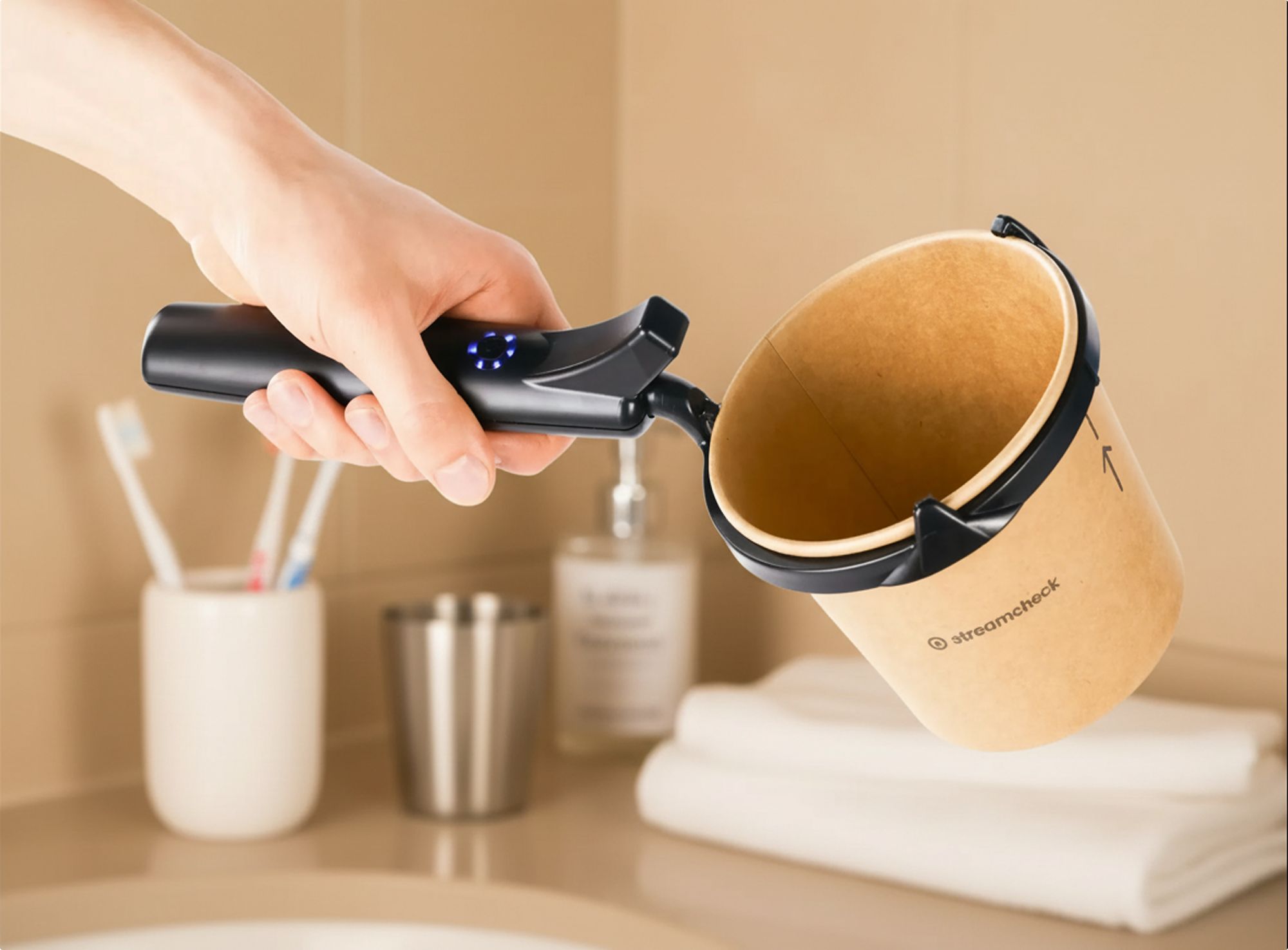 Hand hält Gerät und Becher. Gerät mit Griff und blauen Lichtern. Becher aus braunem Papier.