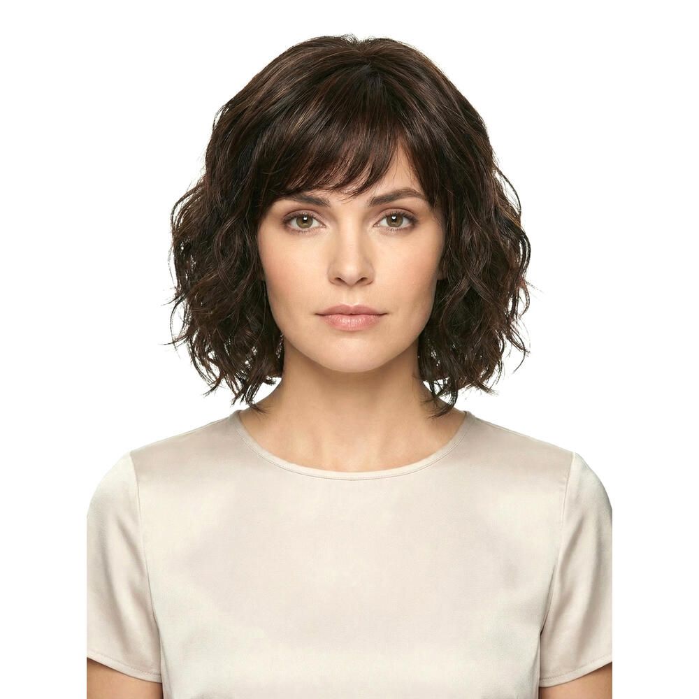 Perücke Capri, braun, gewellt, mit Pony. Frau mit Perücke, Blick in die Kamera. Helles Oberteil.