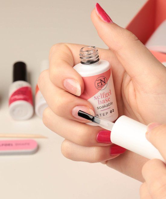 Person hält Flasche mit Pinsel. Aufschrift: selfgel base soakable, STEP 02. PN-Logo. Feile und Holzstab.