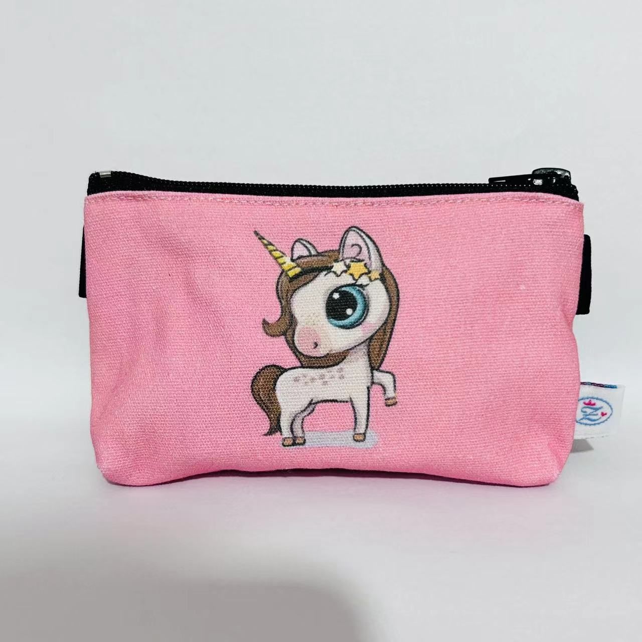 Rosa Tasche mit Einhorn-Motiv. Schwarzer Reißverschluss, schwarze Schlaufen. Kleines Etikett.