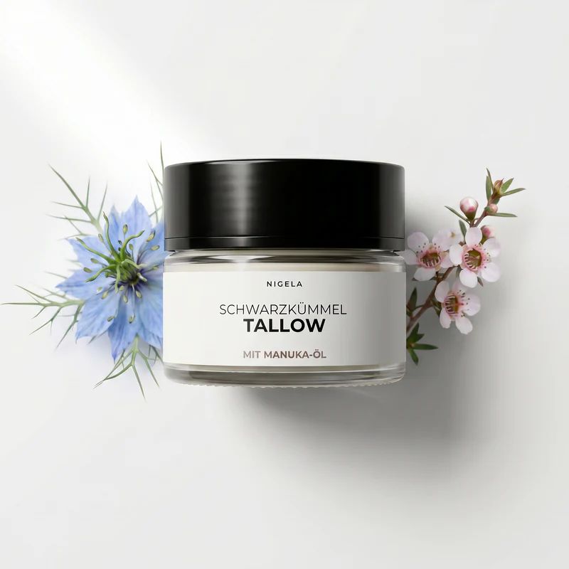 Glas mit schwarzem Deckel, Etikett 'Nigella Schwarzkümmel Tallow mit Manuka-Öl', umgeben von blauen Blüten und Zweigen.